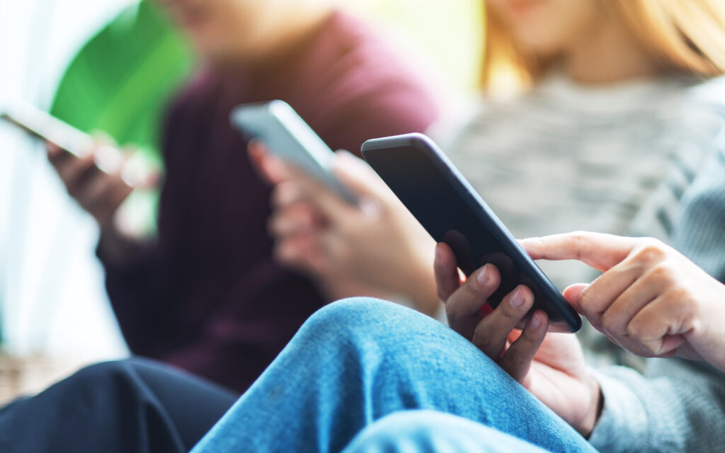 Group of young people using and looking at mobile phone while sitting together
